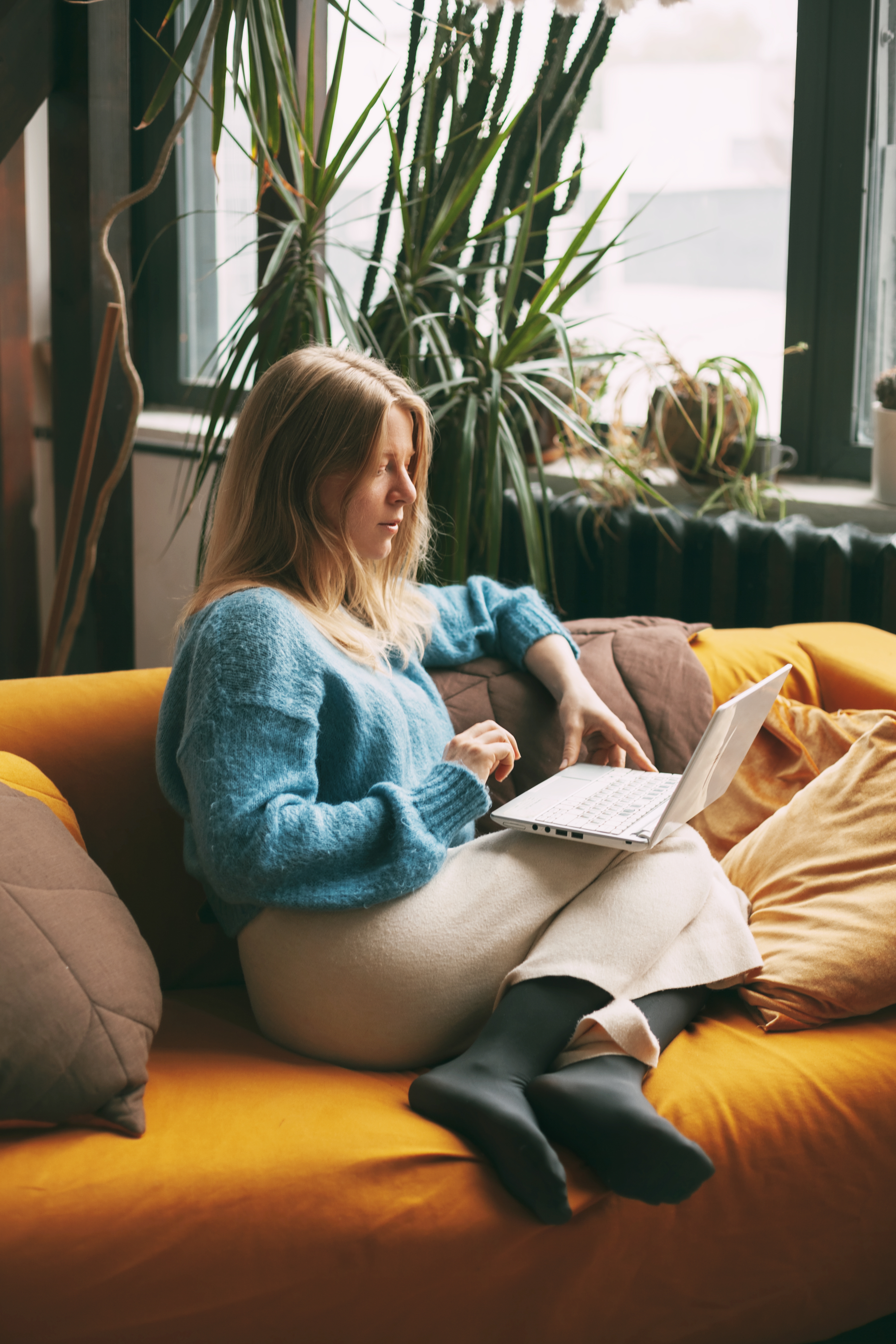 Young woman uses laptop, checks email news online sitting on sofa.
